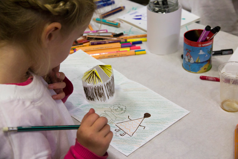 Une jeune participante réfléchi au dessus de son dessin et de son bâtiment colorié.