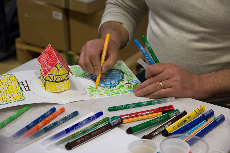 Un participant adulte est en train de colorier au feutre le pop-up en blanc, en maison alsacienne.